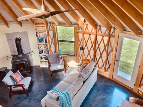 Cozy living space with wooden beams, a fireplace, and modern furniture, featuring large windows and natural light.